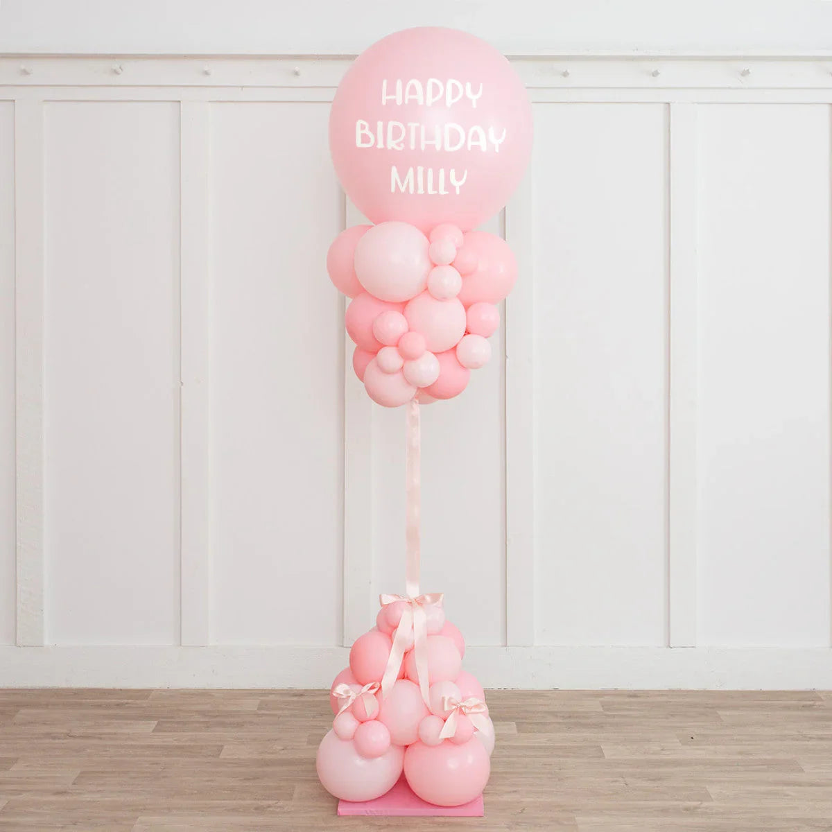 Baby pink balloon pillar with 'Happy Birthday Milly' text, party decoration in Dubai setting