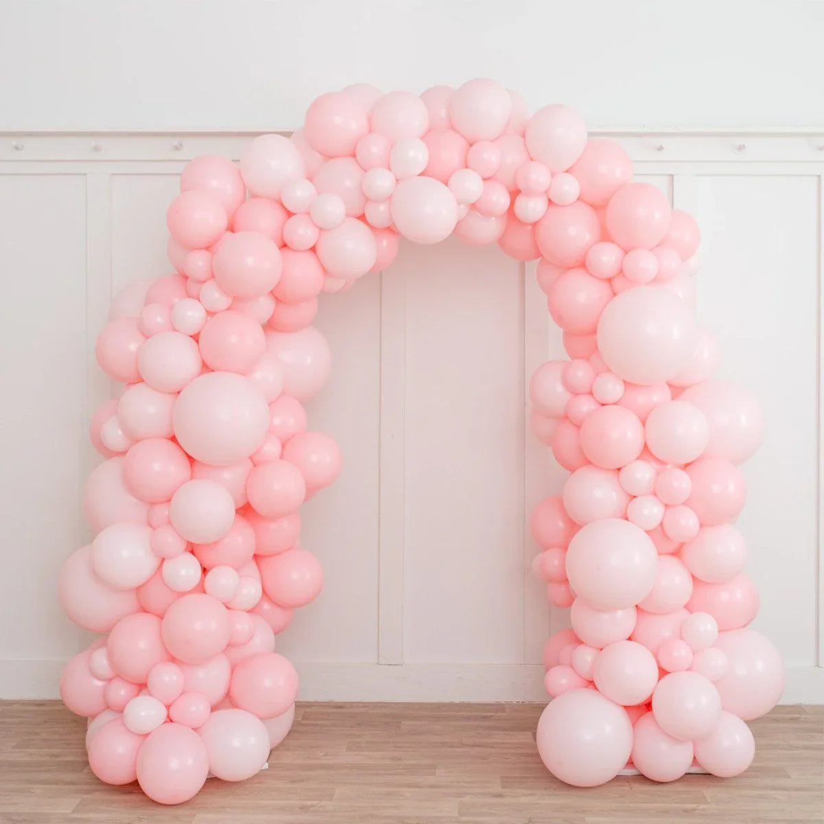 Baby pink balloon arch decoration with various sized balloons in a white room with wooden floor