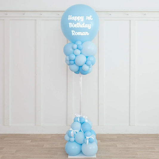 Baby blue balloon pillar for first birthday party with white bows, displayed indoors