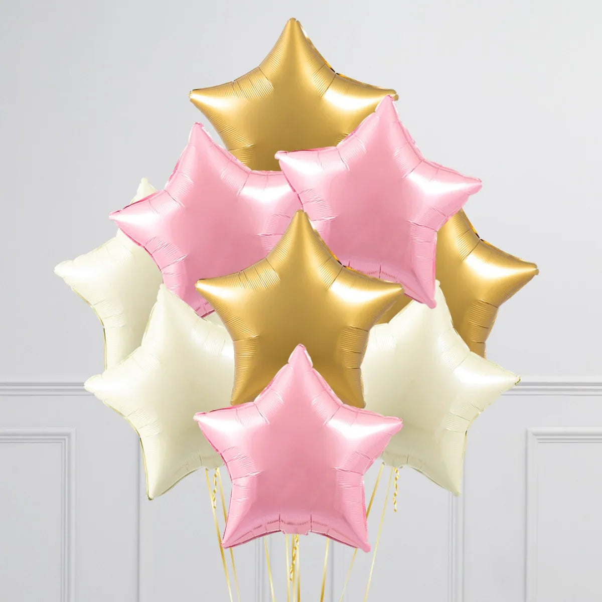 Cluster of inflated star-shaped foil balloons in pink, gold, and white against white wall
