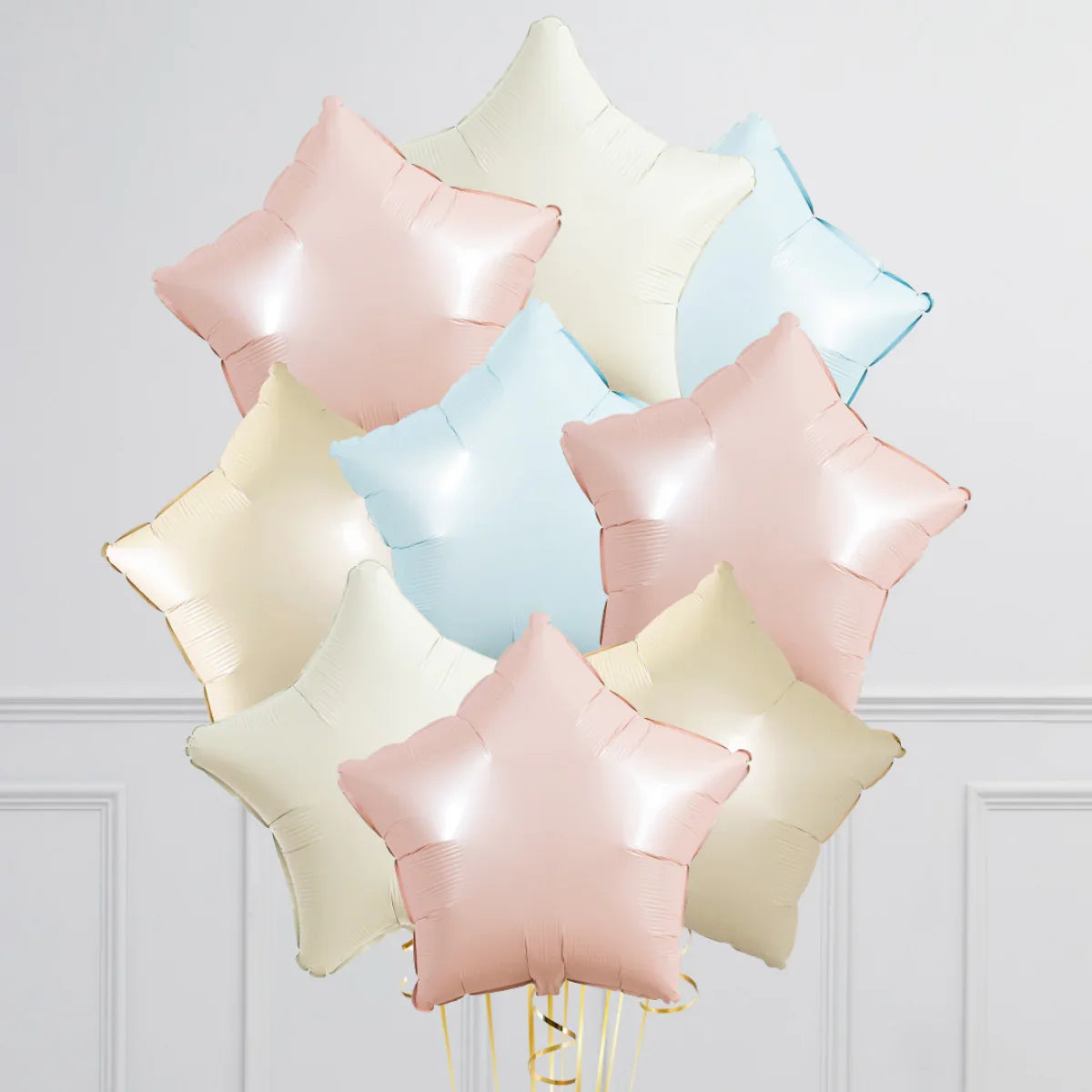 Cluster of pastel star-shaped foil balloons in pink, blue, and cream against white wall
