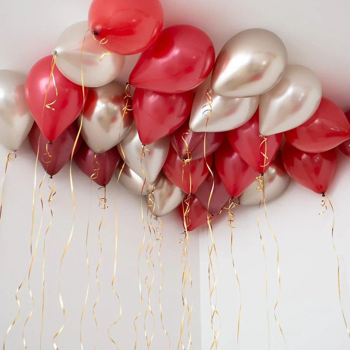 Deep red and pearl balloons with gold ribbons floating against white ceiling corner