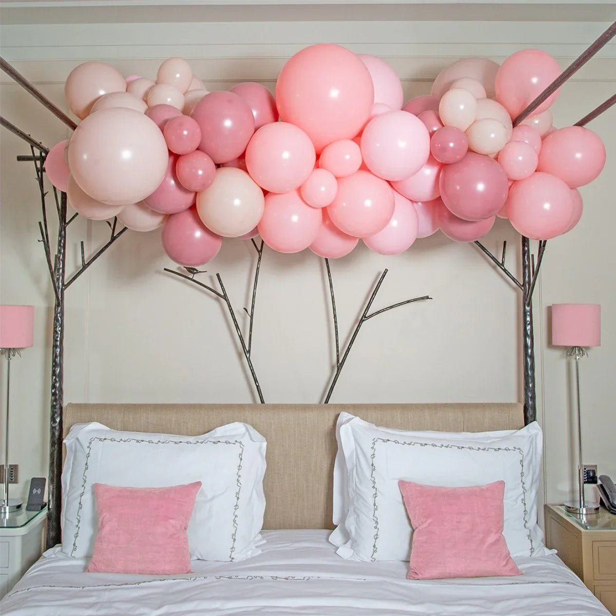 Pink cherry blossom balloon garland decoration over beige bed with white bedding and pink pillows
