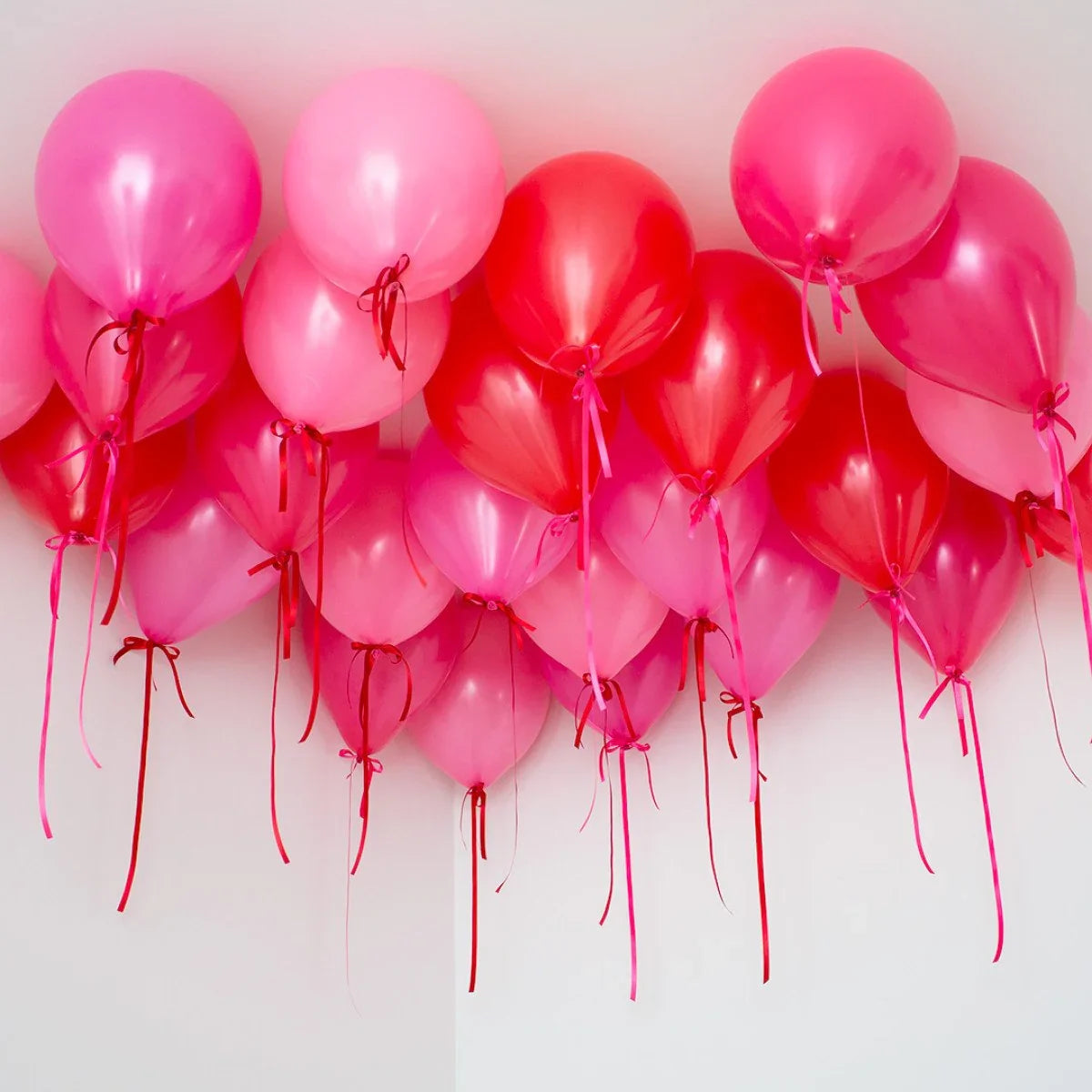 Cluster of helium pink and red balloons tied with ribbons floating near the ceiling
