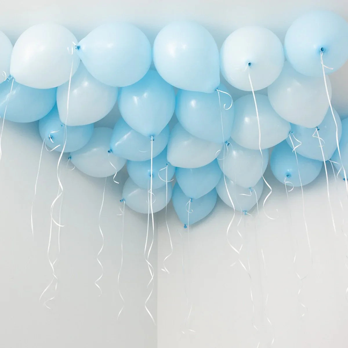 Cluster of baby blue balloons attached to white ceiling with curling white ribbons