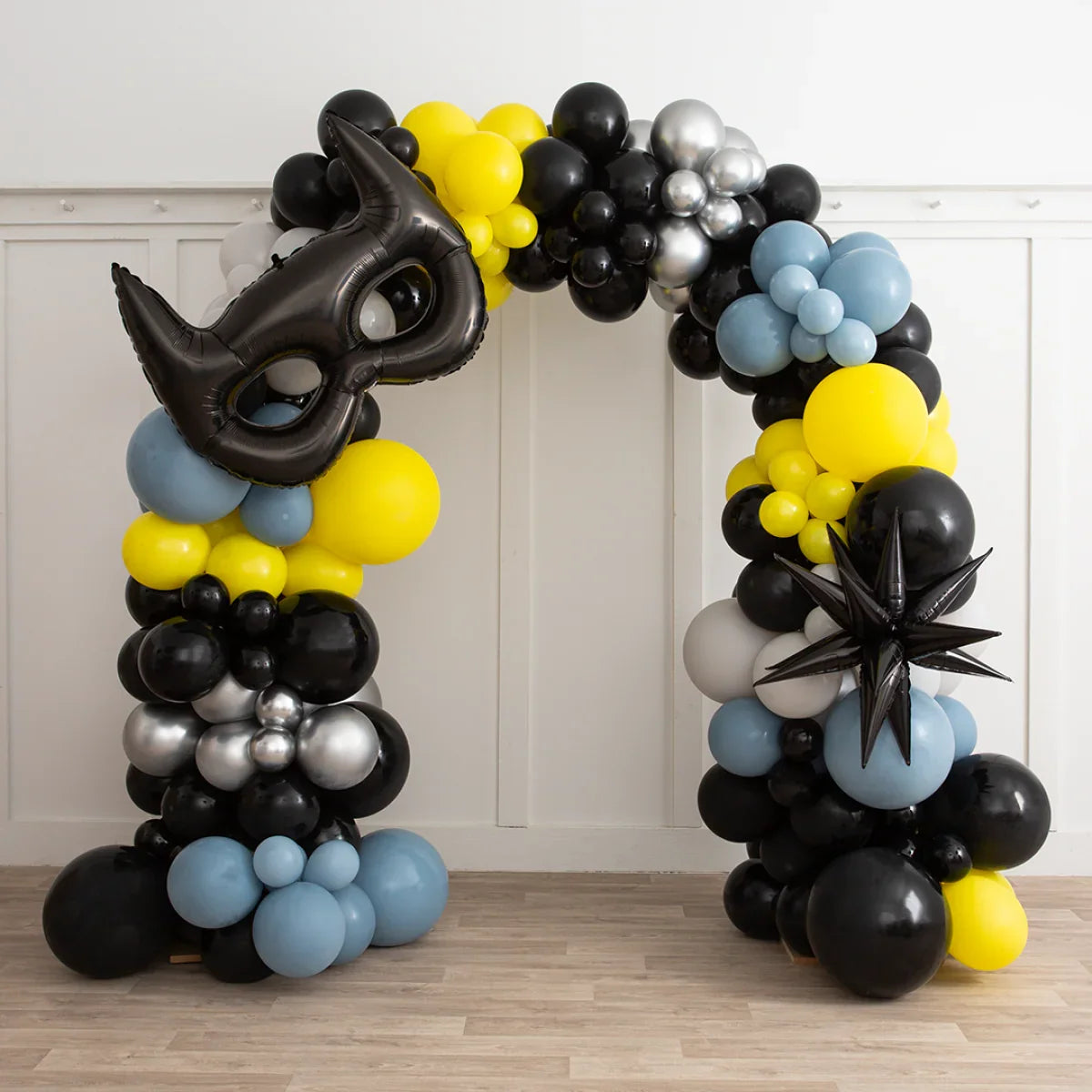 Black, yellow, silver, and blue balloon arch with Batman mask and star decorations indoors