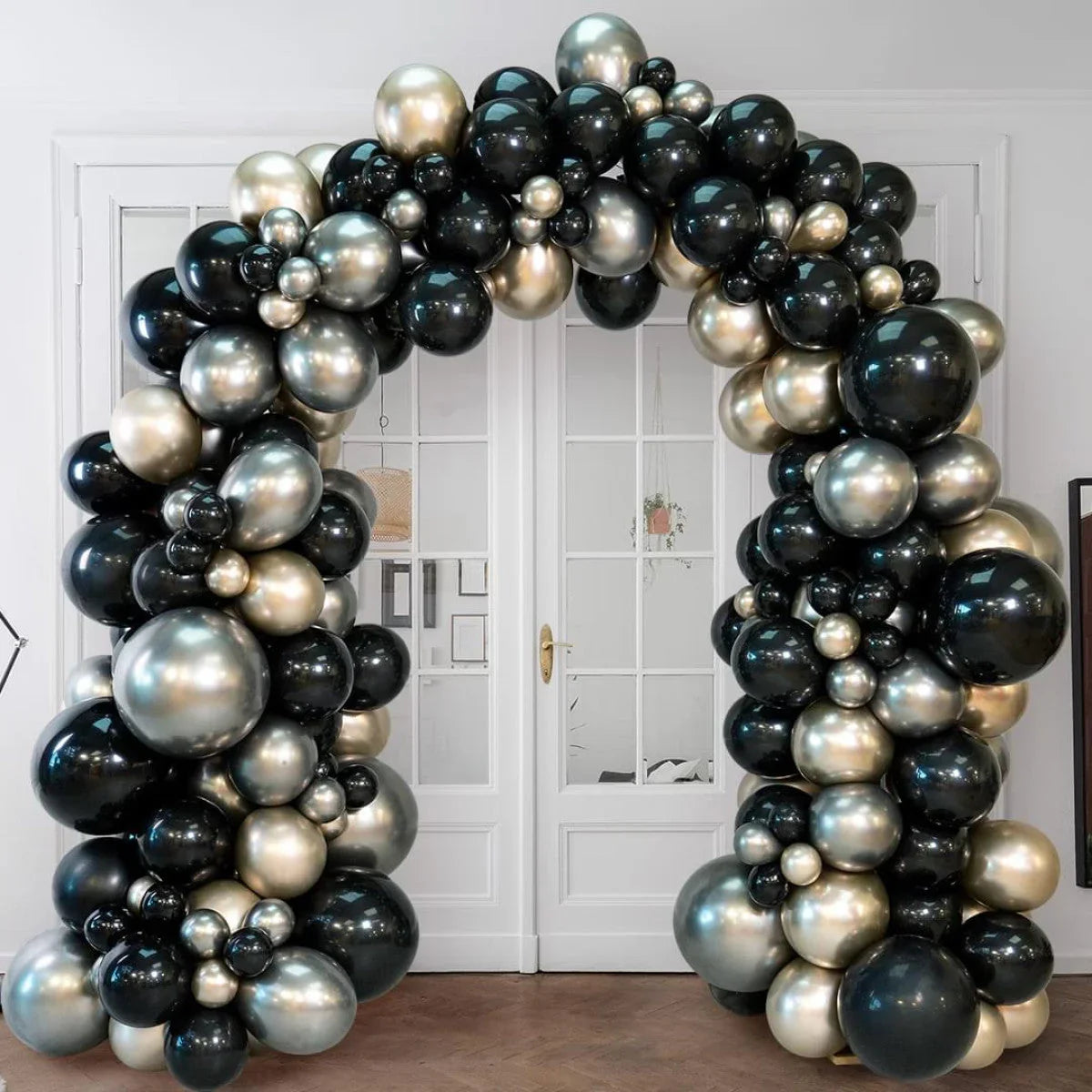 Black, silver, and gold balloon arch decoration in front of white double doors indoors