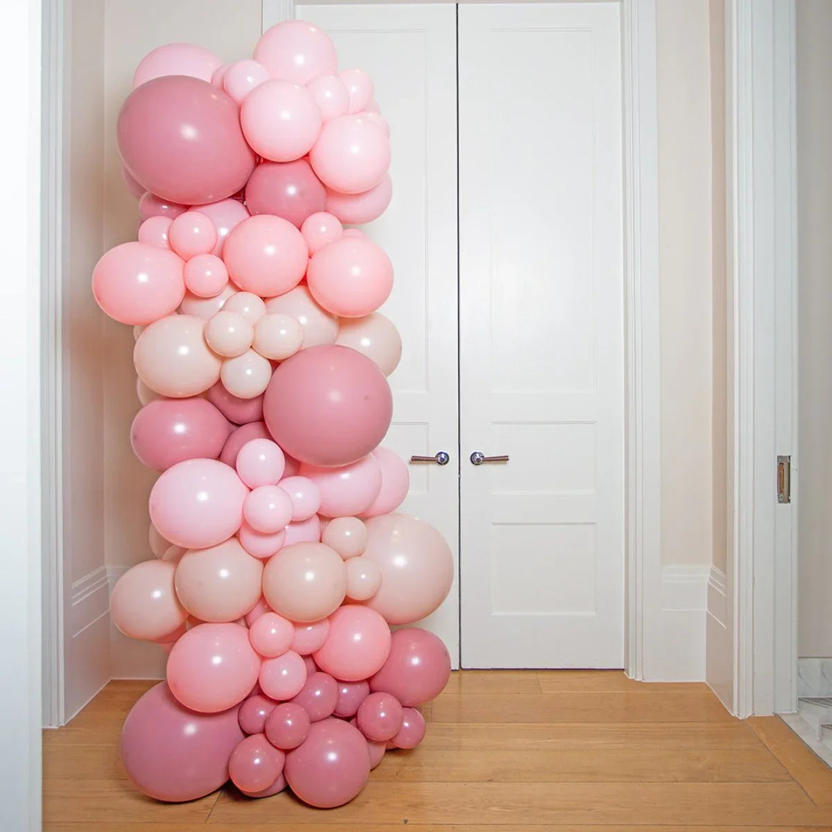 Tall pillar made of clustered pink and blush balloons in front of white double doors indoors