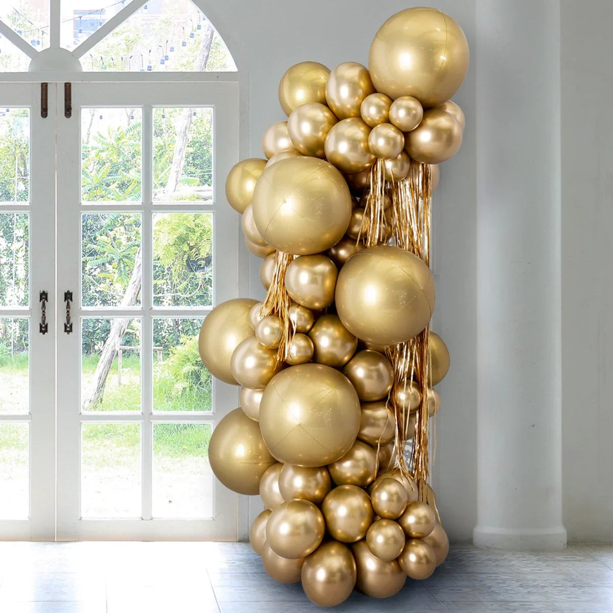 Tall pillar decoration made of gold metallic balloons of various sizes indoors near glass doors