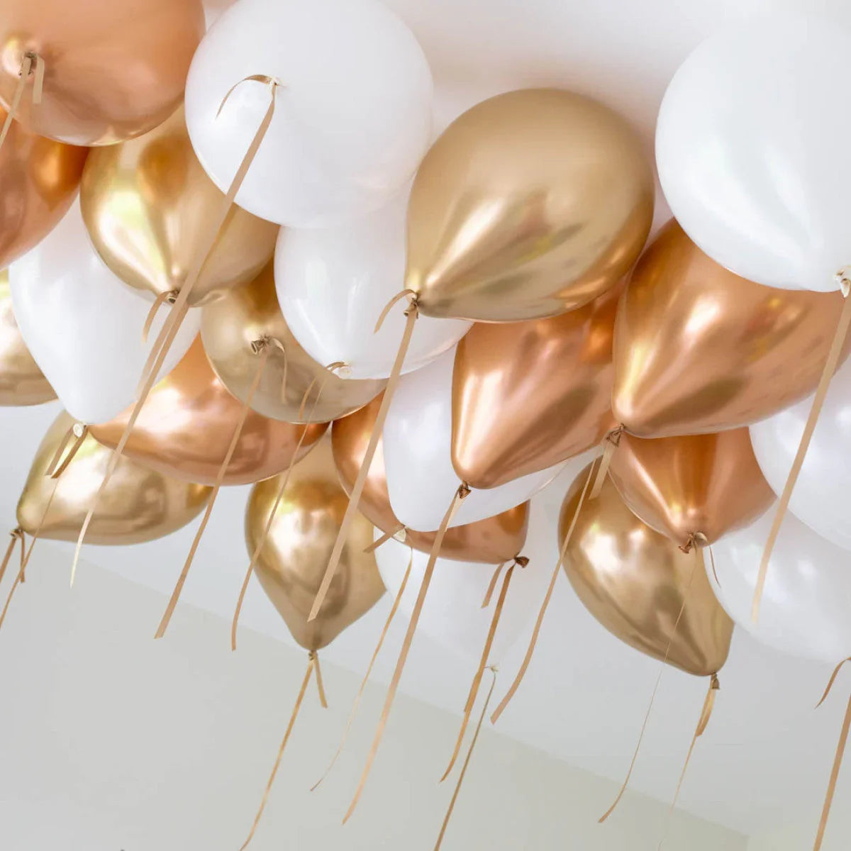 Cluster of metallic copper, gold, and white balloons floating against a white ceiling