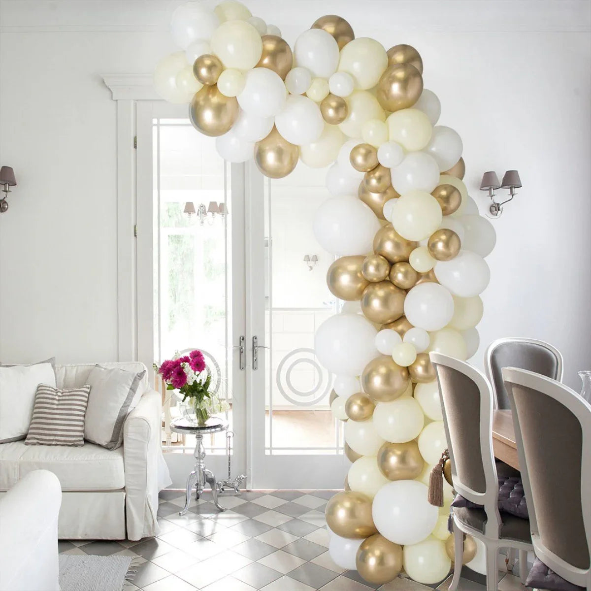 Ivory, cream, and gold balloon arch decorating a bright living and dining room with white furniture