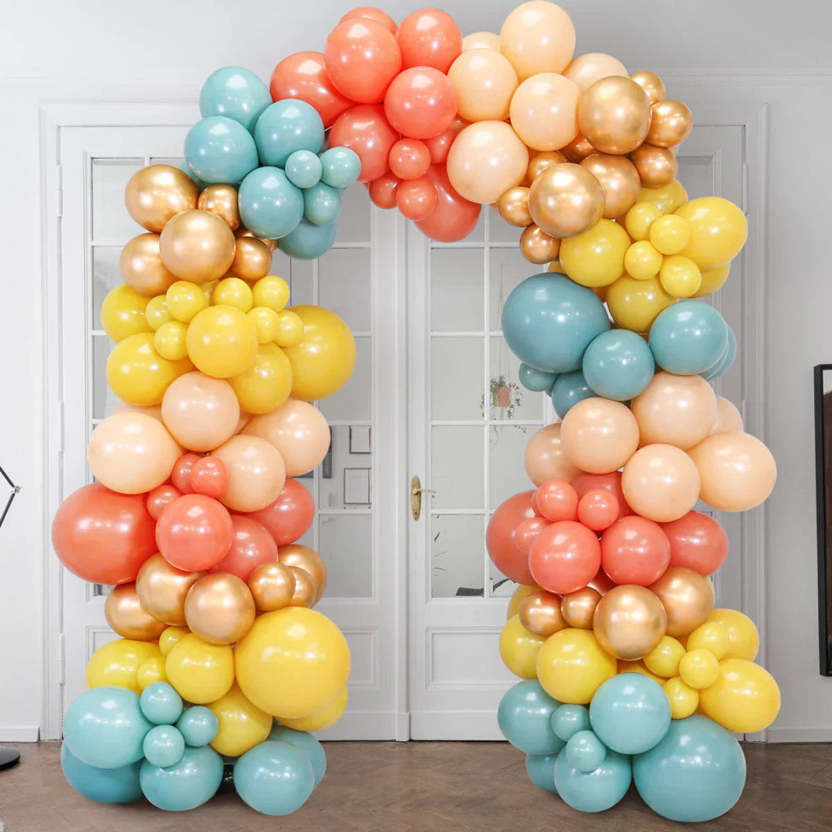 Colorful balloon arch with peach, yellow, teal, and gold balloons in indoor party setting