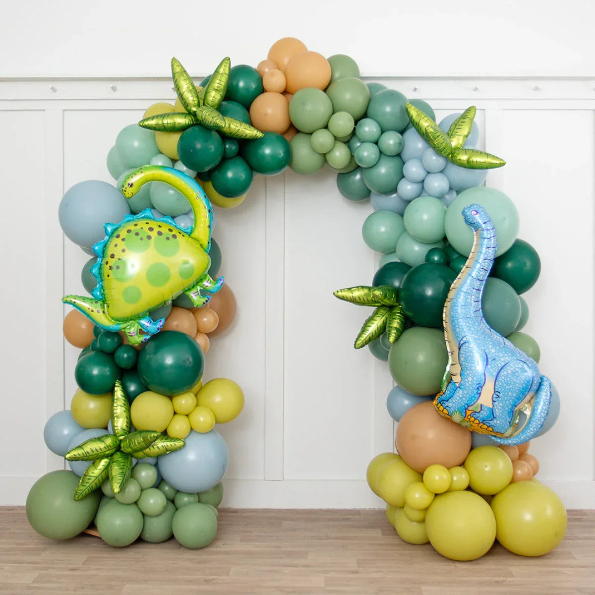 Dinosaur-themed balloon arch with green, blue, and beige balloons and foil dinosaur and leaf accents