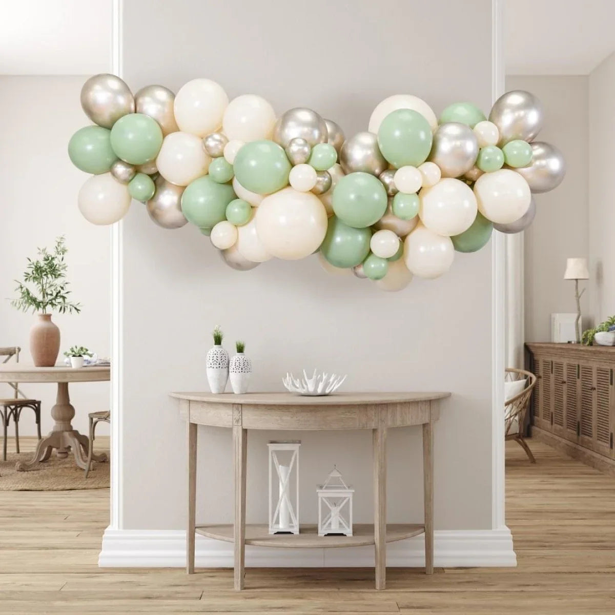 Balloon garland in sage green, cream, and silver hanging above a wooden console table in a modern living room