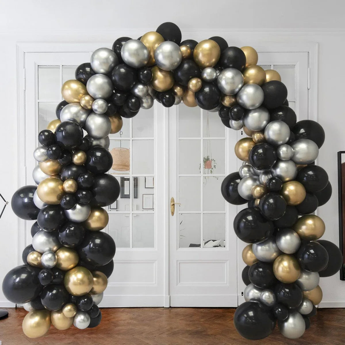 Balloon arch decoration with black, gold, and silver balloons in a bright room with white double doors