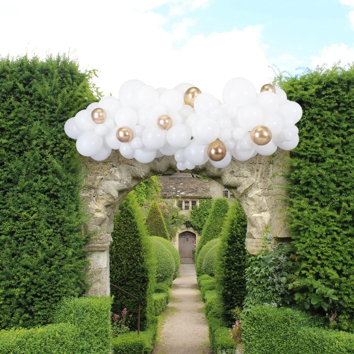 White and gold balloon garland decoration on stone archway in lush garden pathway