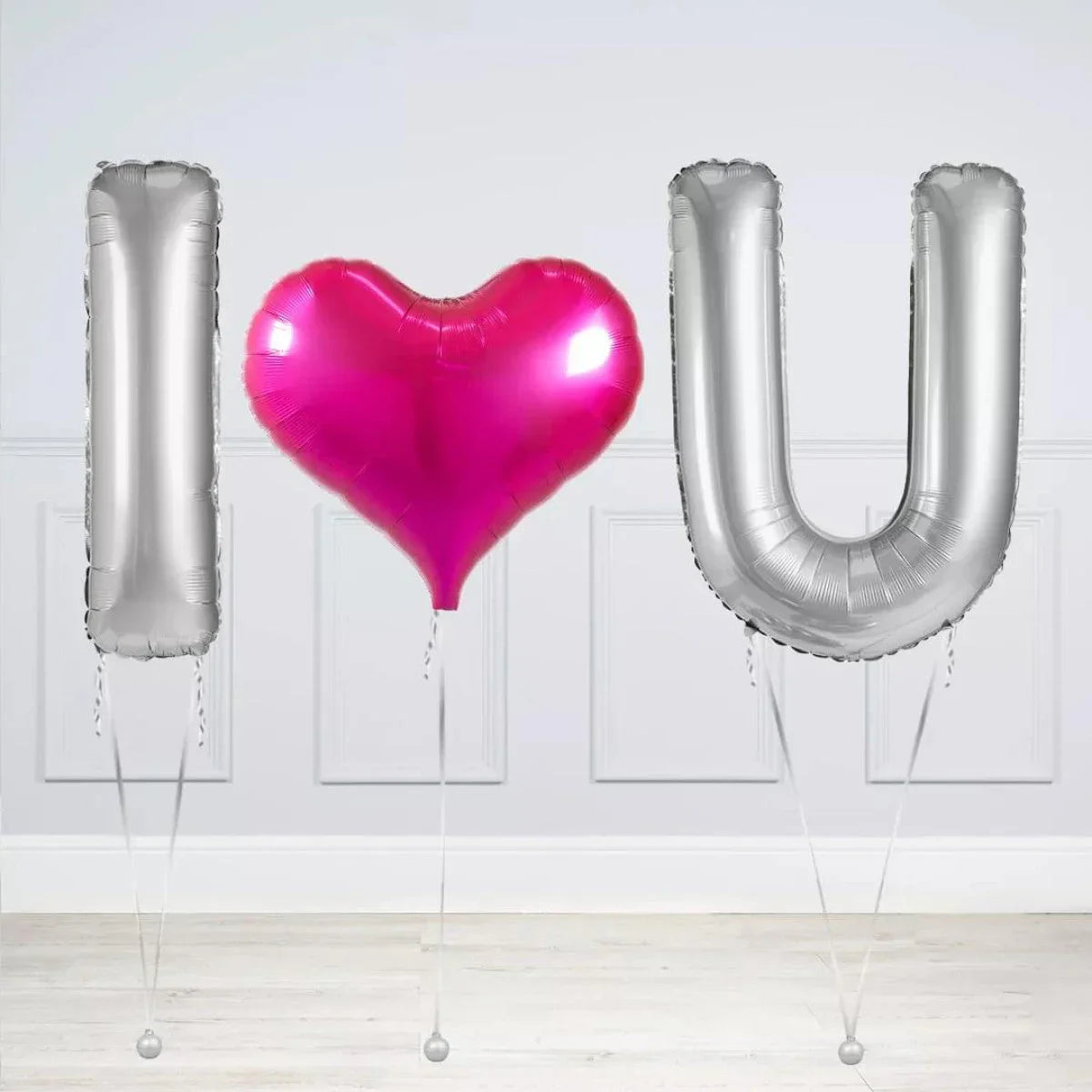Silver metallic I and U balloons with a pink heart-shaped balloon in the middle on white background