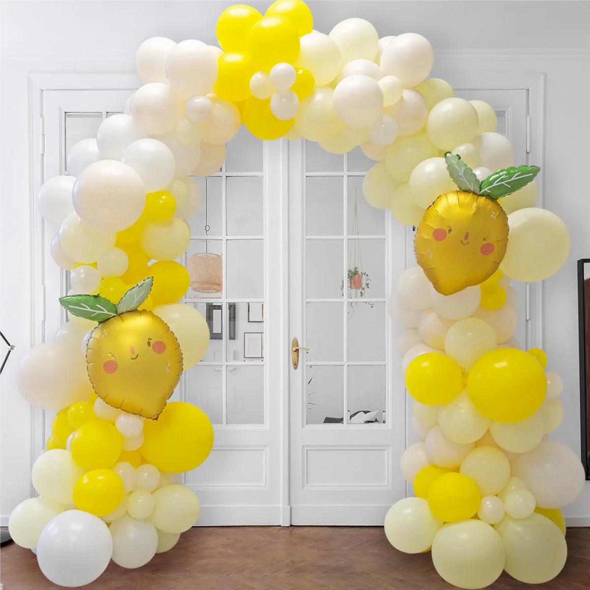 Yellow and white balloon arch decorated with two smiling lemon-shaped foil balloons in a bright room