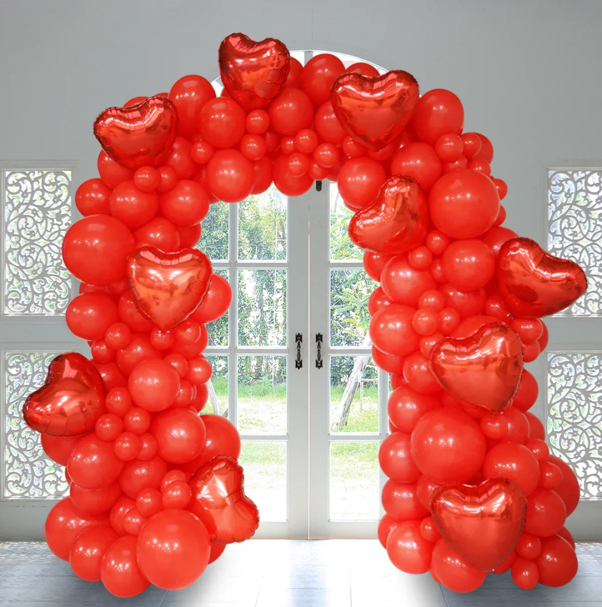 Red balloon arch with assorted round balloons and metallic heart-shaped balloons in front of white French doors