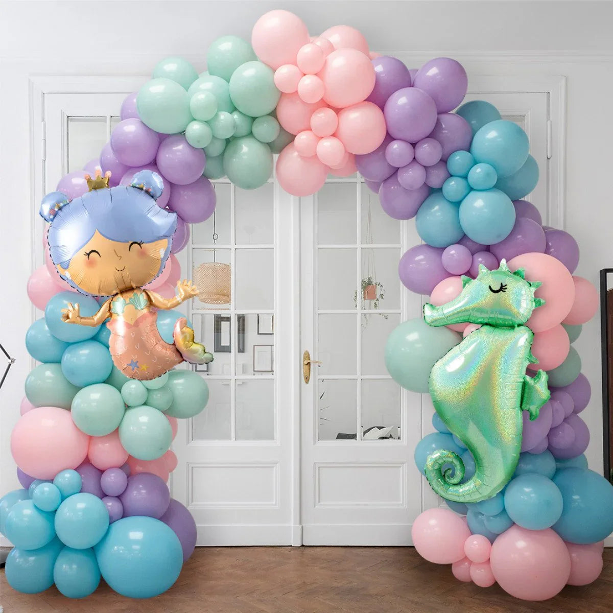 Colorful balloon arch with mermaid and seahorse balloons decorating white double doors indoors