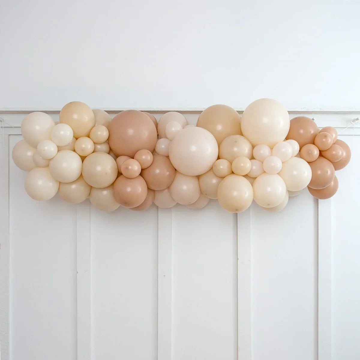 Neutral beige balloon garland decoration on white paneled wall for events