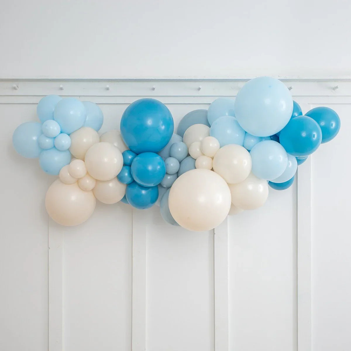 Decorative balloon garland in shades of blue and cream hanging on white wall