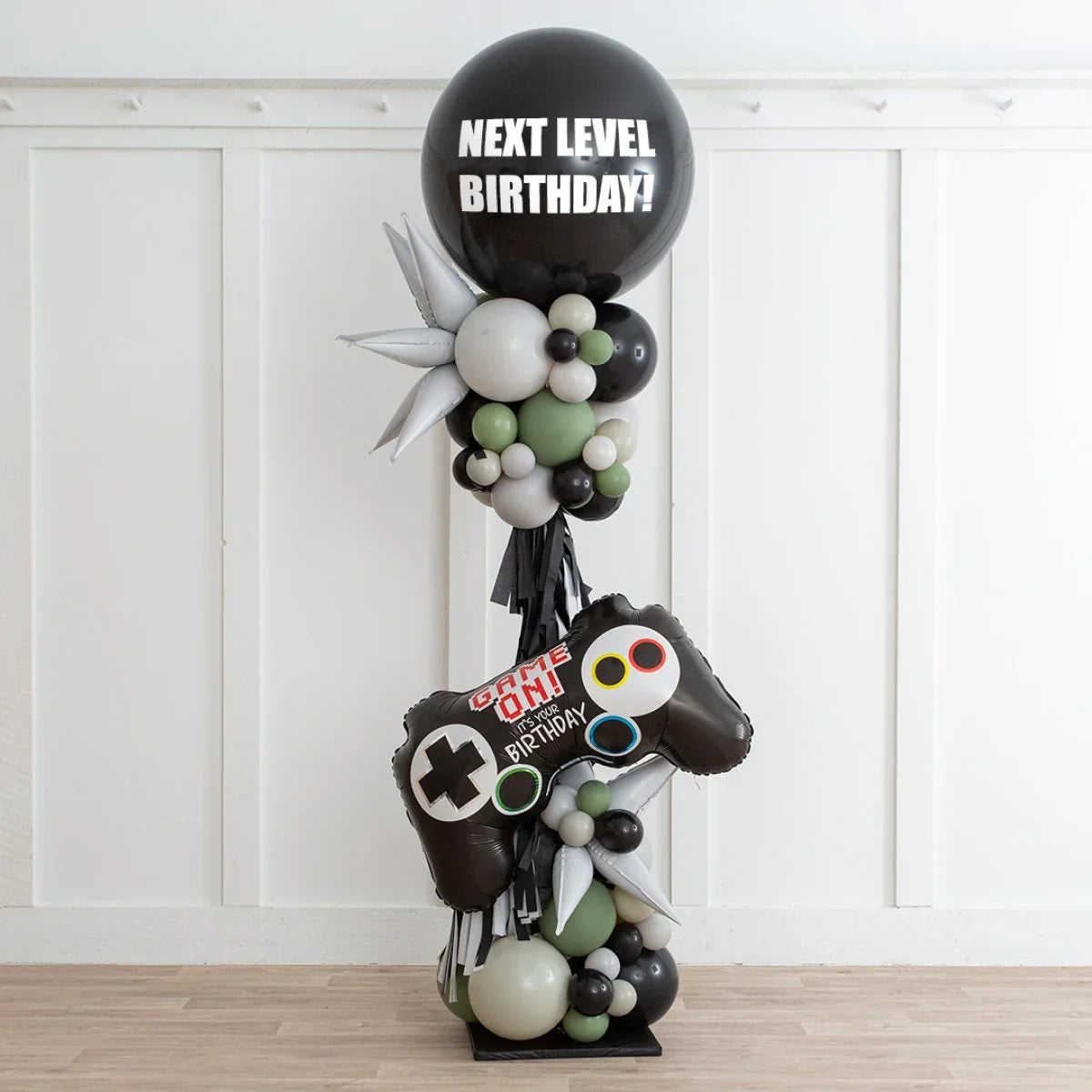 Birthday balloon pillar decoration with a black round balloon saying Next Level Birthday and a game controller shaped balloon