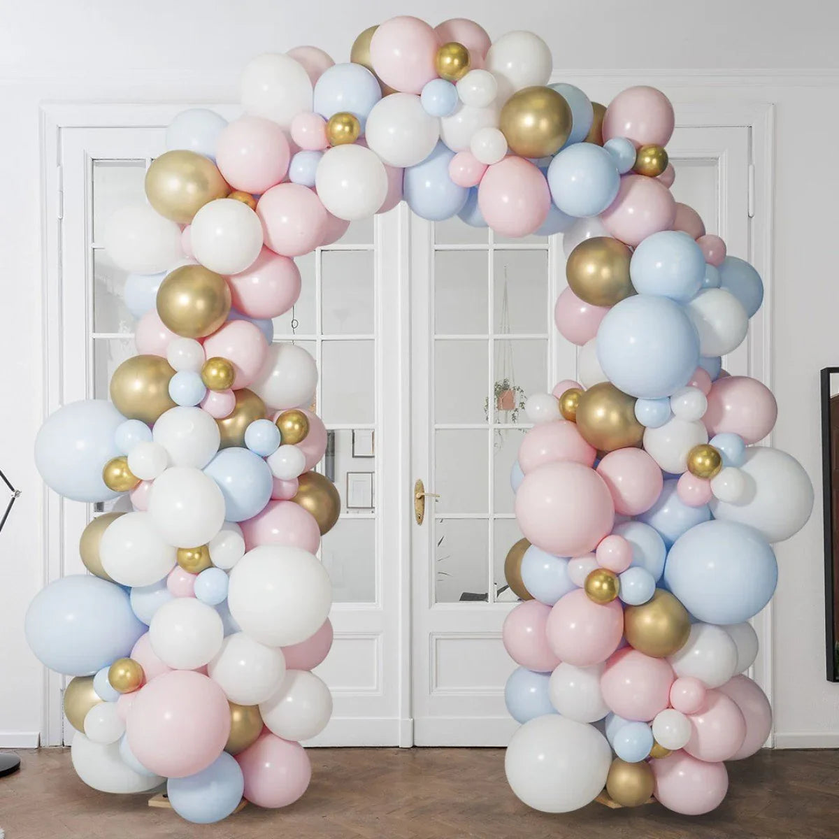 Decorative balloon arch in pastel pink, blue, white, and gold inside a stylish room with white doors