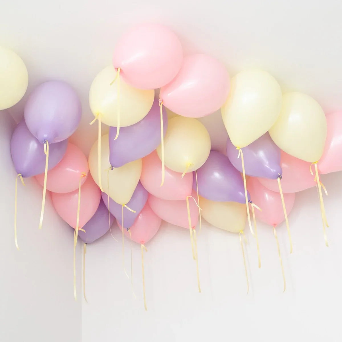 Pastel pink, purple, and cream balloons floating on a white ceiling for party decoration