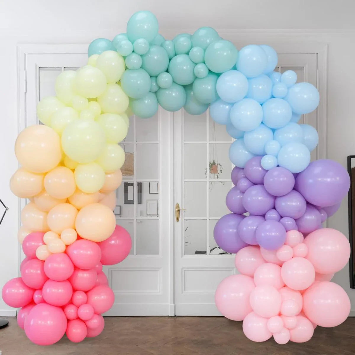 Pastel rainbow balloon arch with pink, purple, blue, green, yellow, and peach balloons indoors
