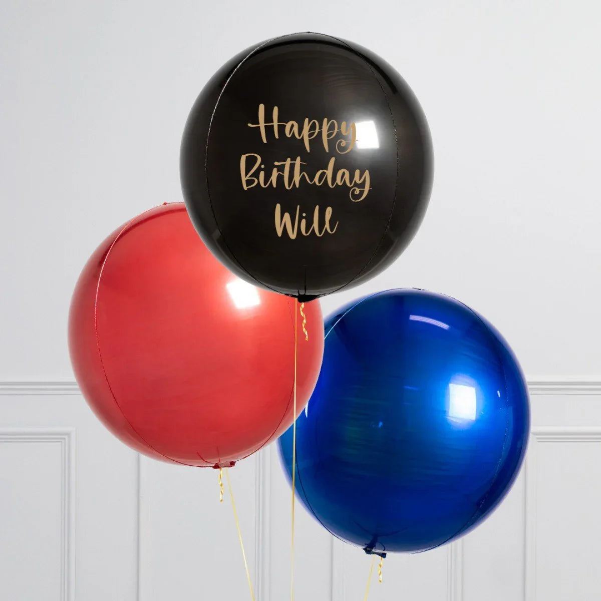 Personalized black balloon with gold Happy Birthday Will text, alongside red and blue balloons