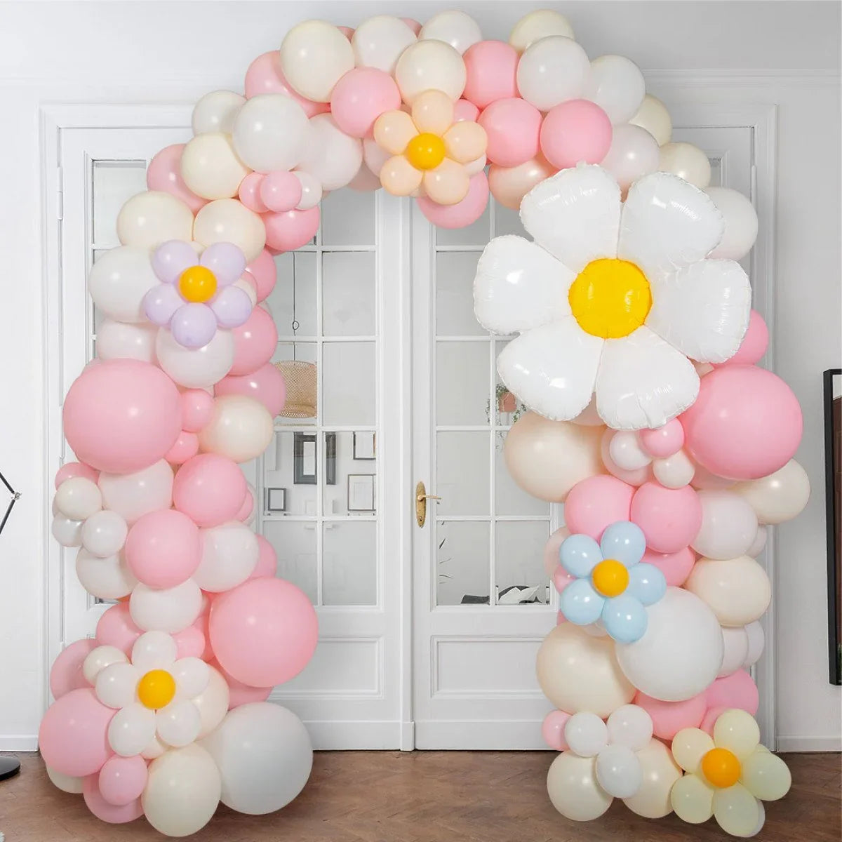 Pink pastel balloon arch with daisy-shaped balloons in front of white double doors