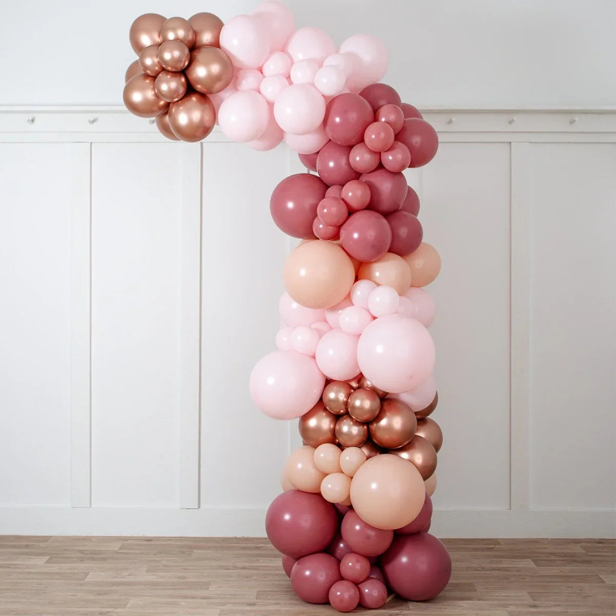 Rose gold and pink asymmetric balloon arch decoration against white wall indoors