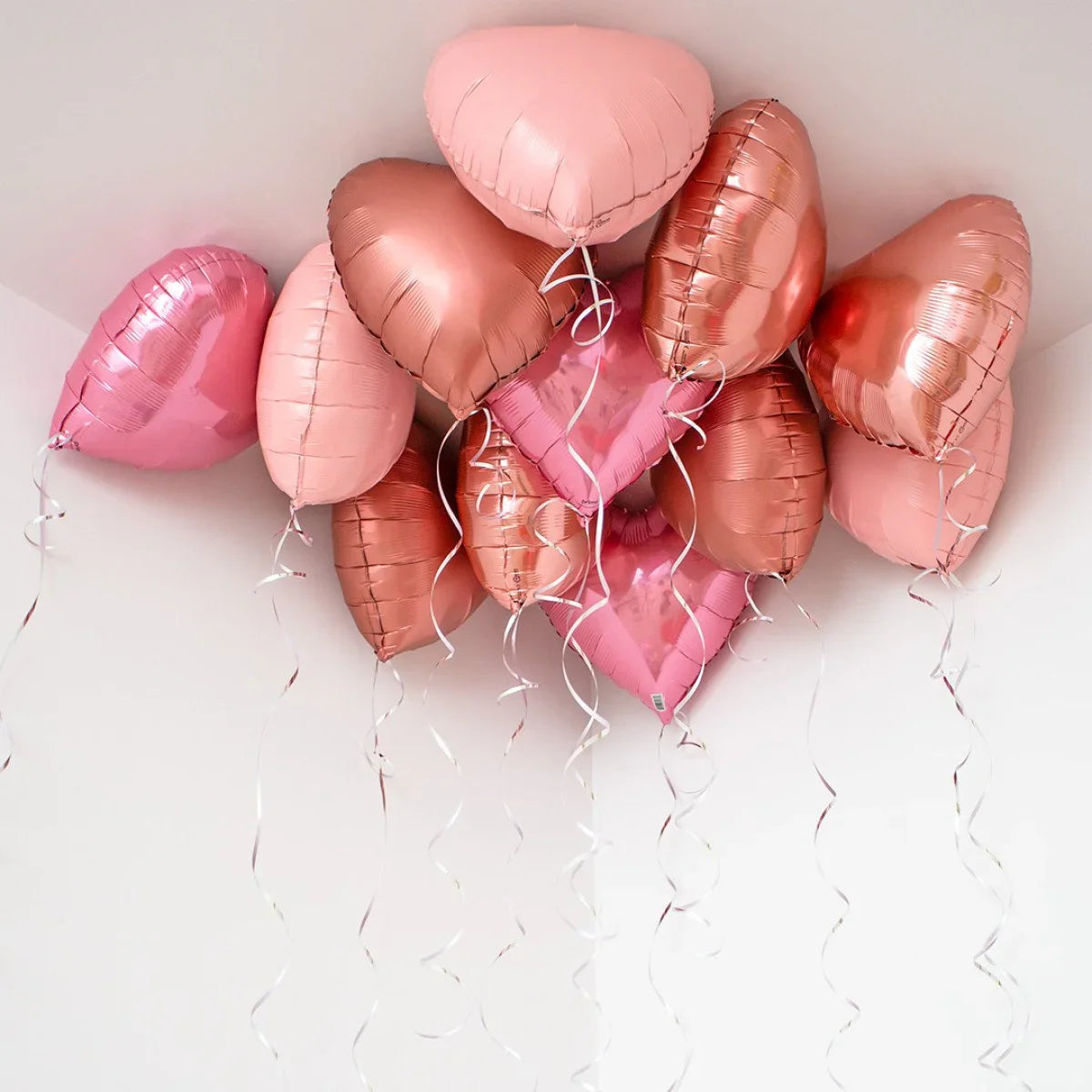 Cluster of rose gold and pink heart-shaped helium balloons floating near white ceiling