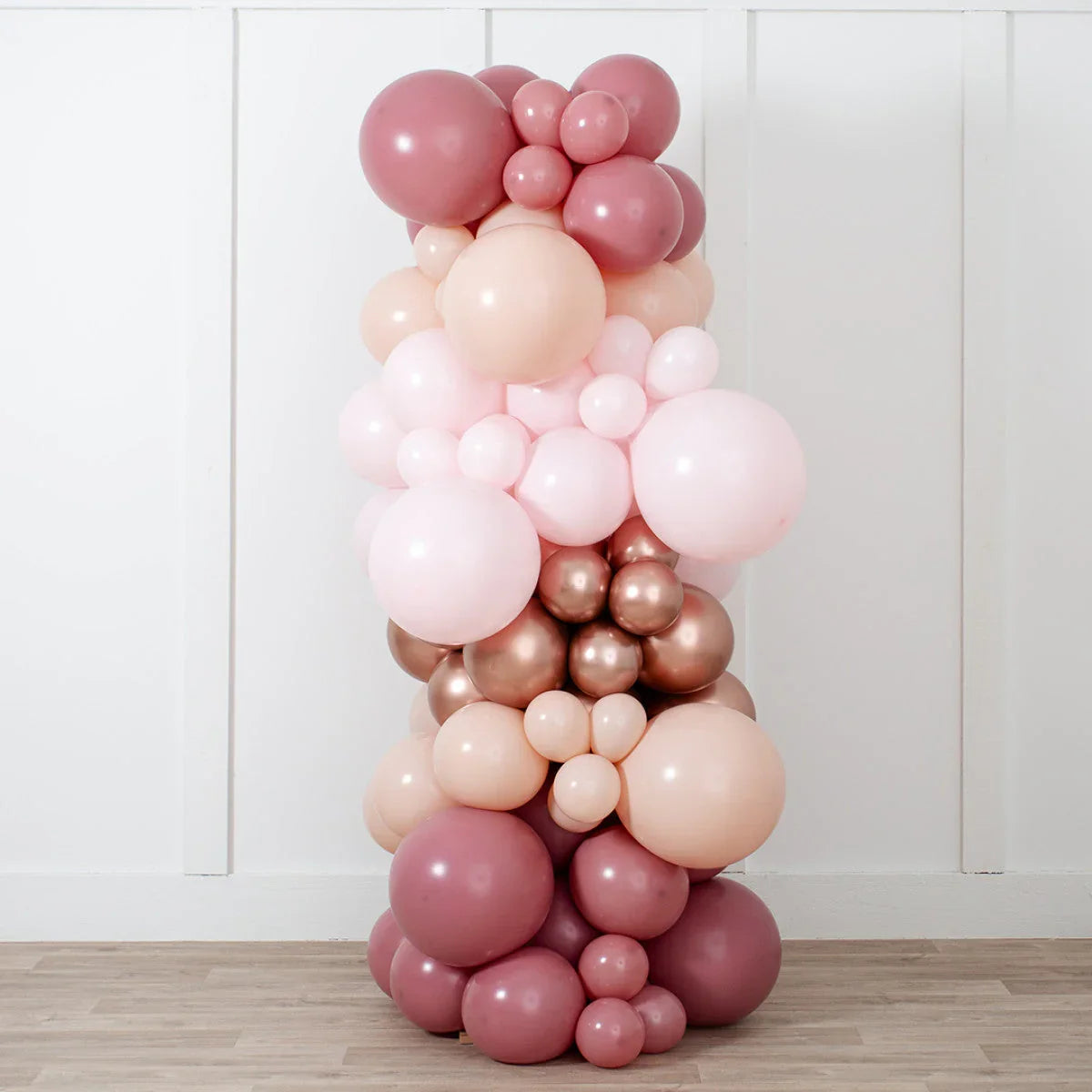 Tall balloon pillar decoration in rose gold, blush pink, and light pink shades against white wall