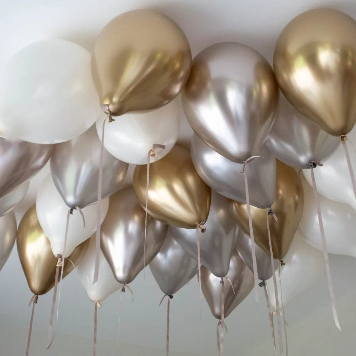 Helium balloons in gold, silver, and white hanging from a ceiling with ribbons