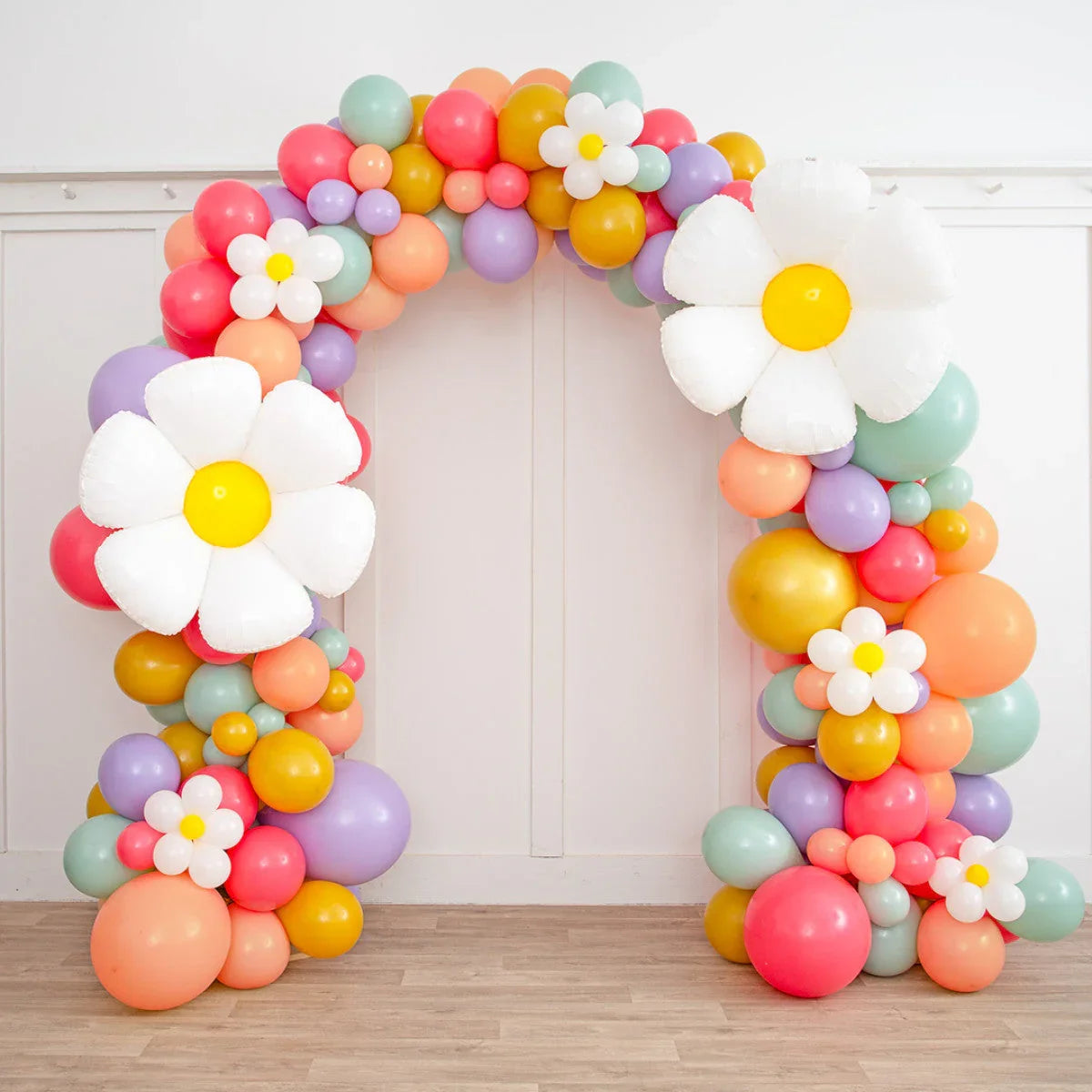 Colorful balloon arch with large white daisy balloons on wooden floor indoors