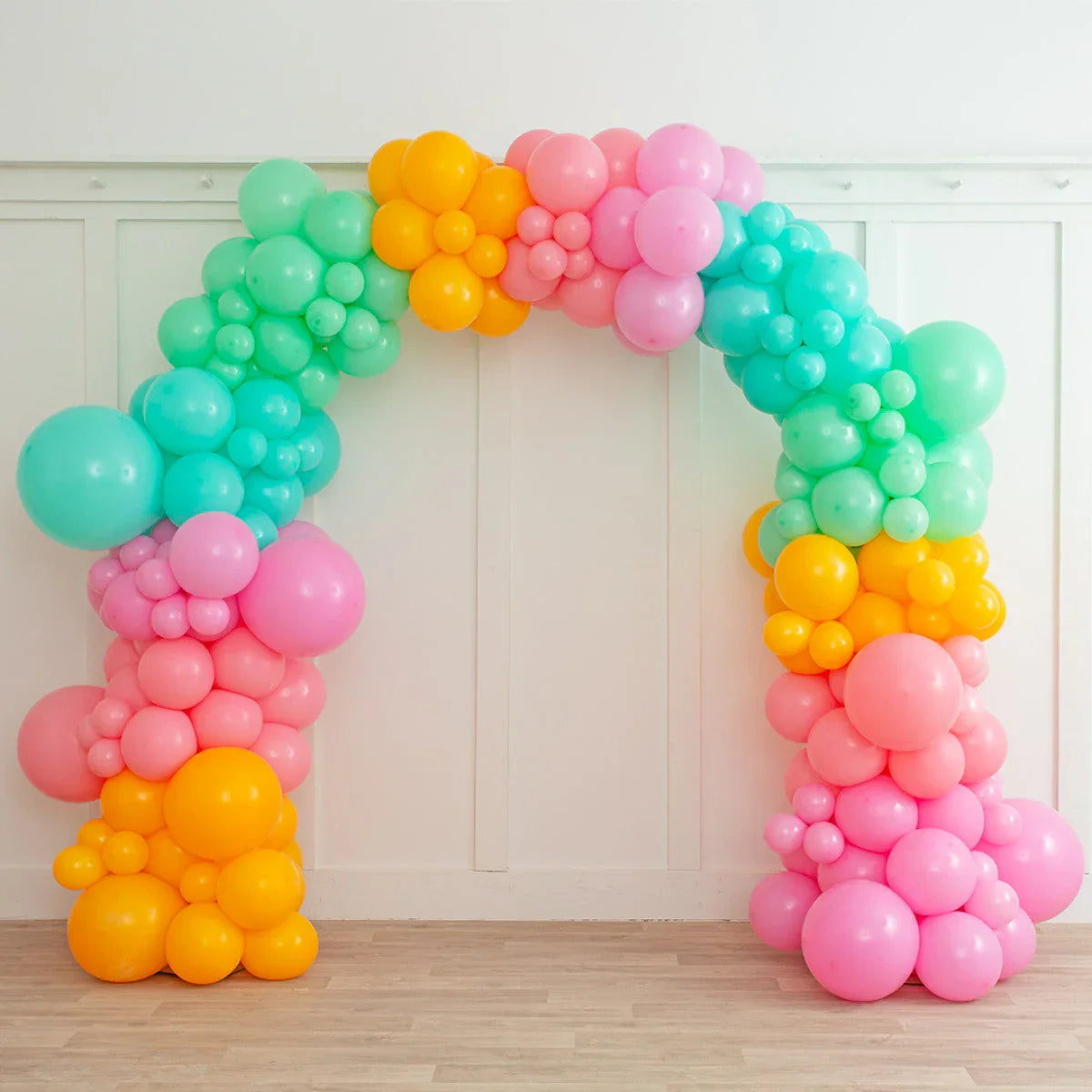 Colorful balloon arch in pastel pink, green, blue, and yellow against white paneled wall