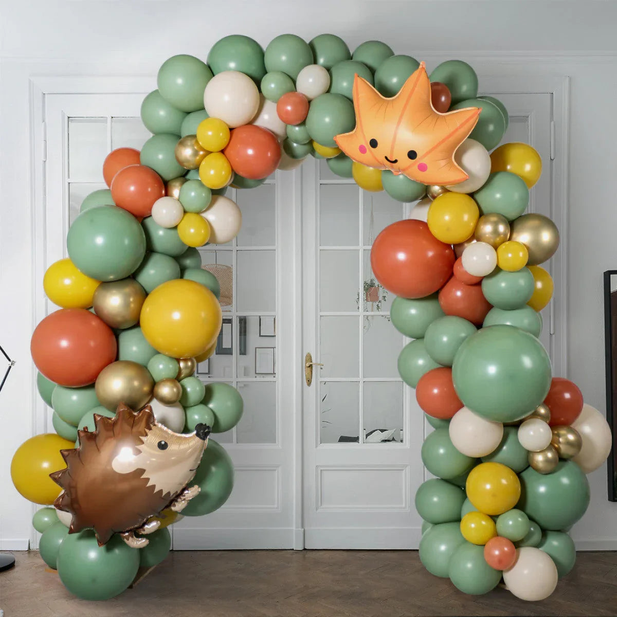 Woodland themed balloon arch with green, yellow, orange, cream and gold balloons, decorated with hedgehog and leaf foil balloons