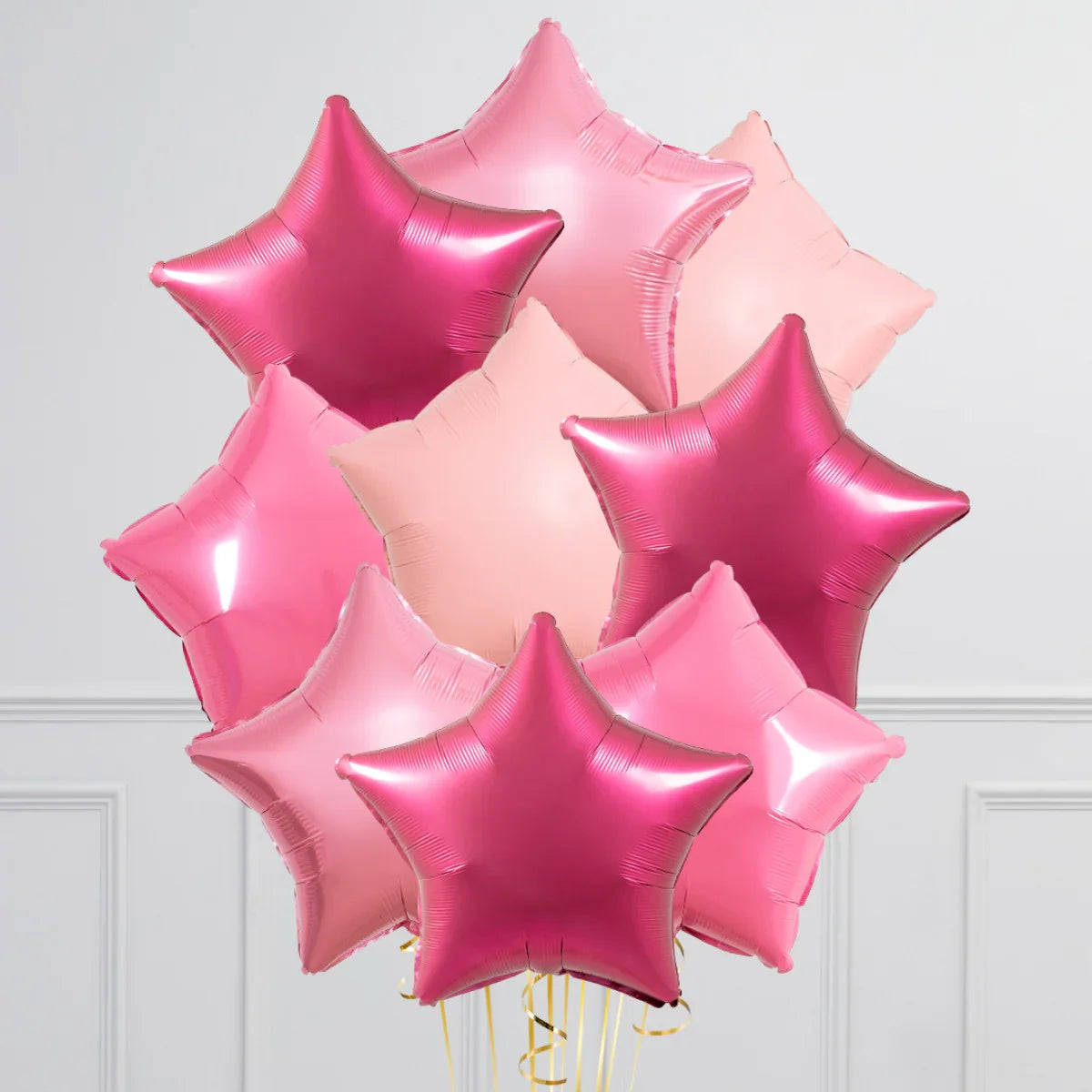Bunch of inflated star-shaped foil balloons in various shades of pink against a white wall