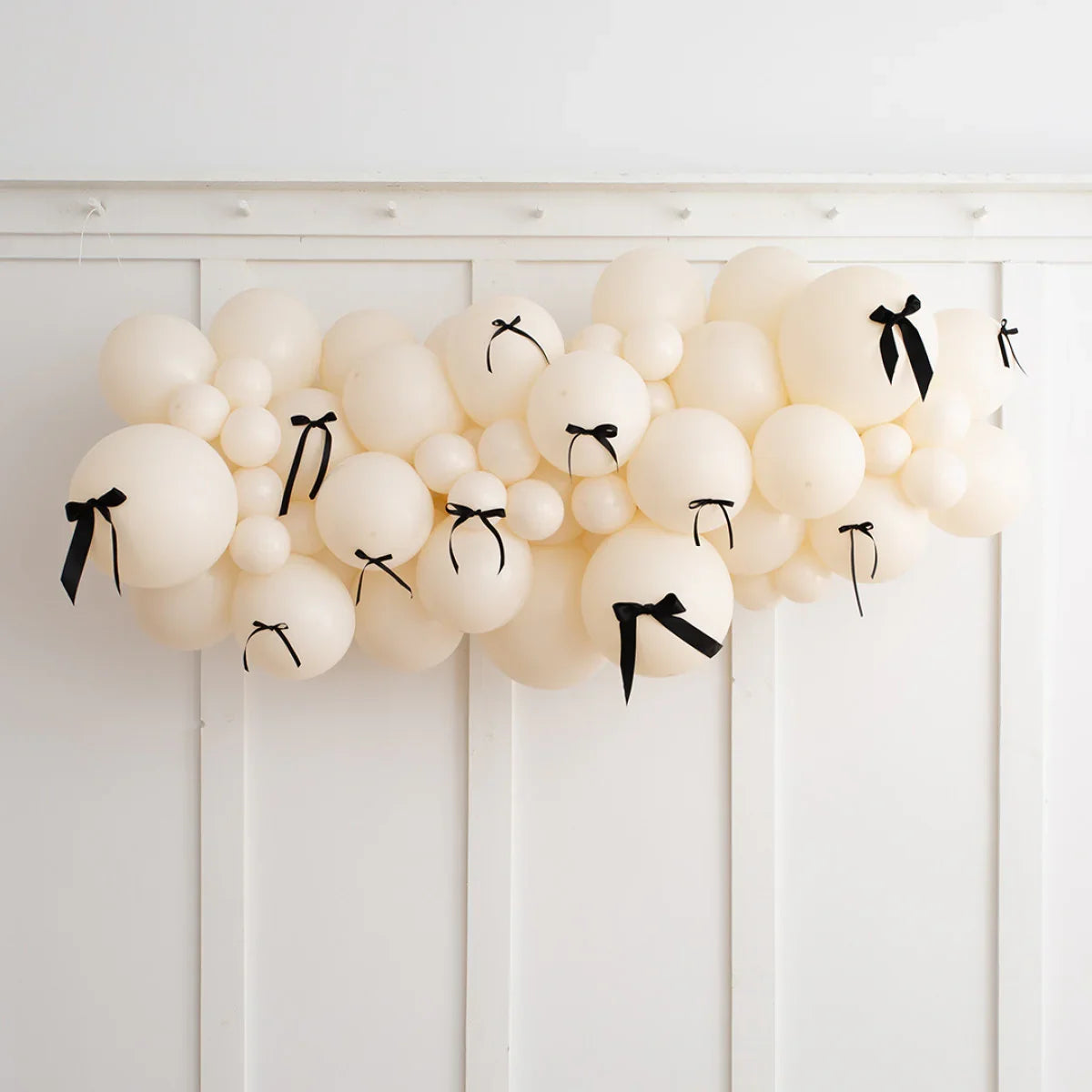 Ivory balloon garland with black bows decorating white paneled wall for elegant event