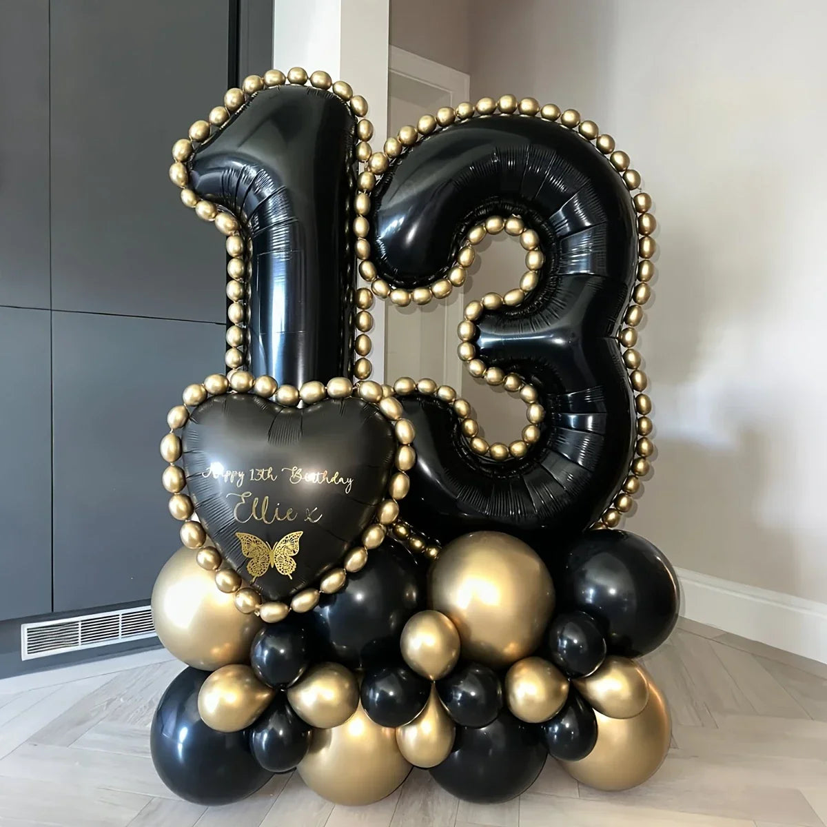 Black and gold balloon arrangement with large number 13 and heart-shaped balloon reading Happy 13th Birthday Ellie x