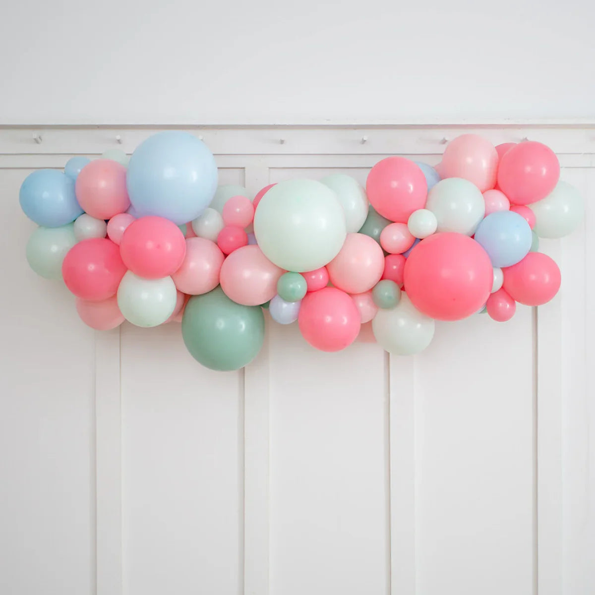 Colorful balloon garland in pastel pink, blue, green, and white, hung on white paneled wall