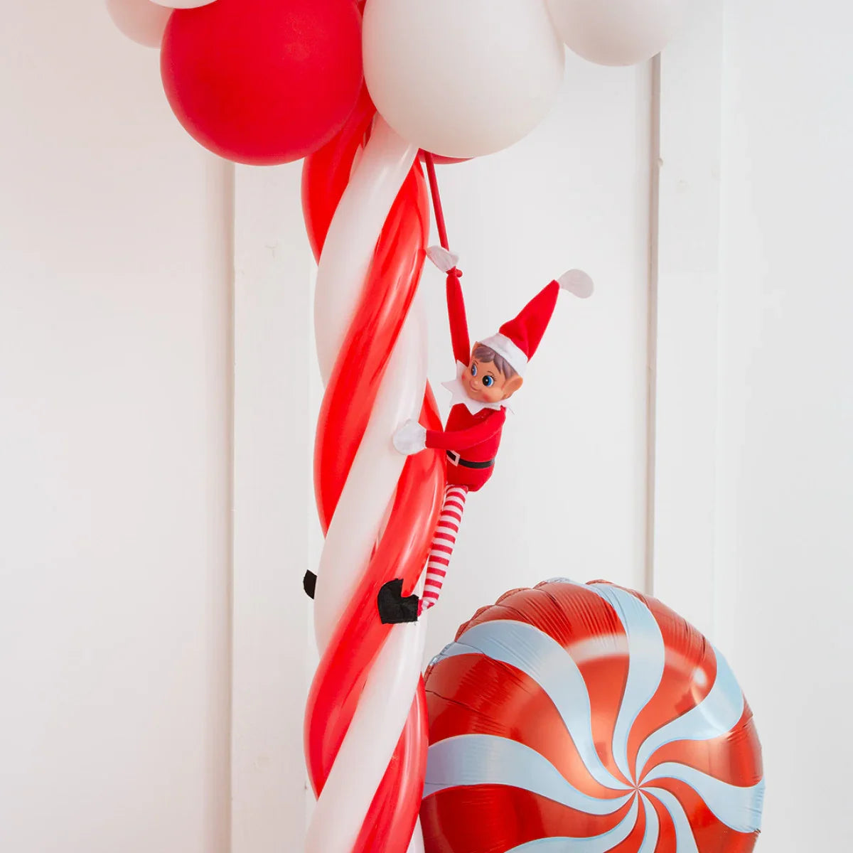 Christmas elf doll climbing red and white balloon pillar with large peppermint swirl balloon