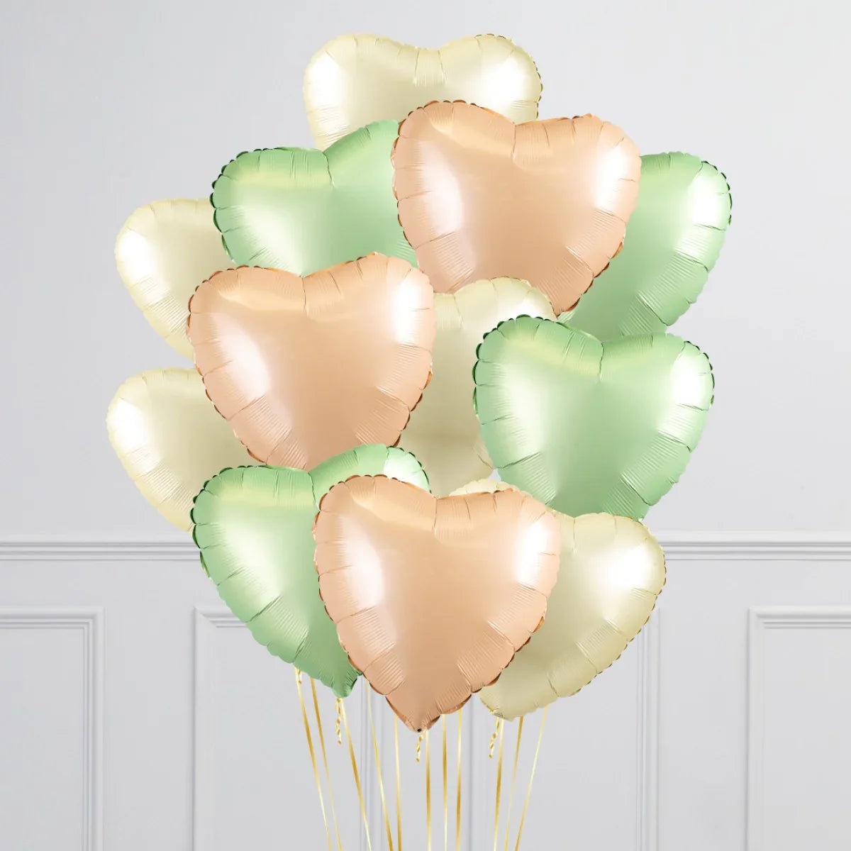 Bunch of shiny inflated heart-shaped foil balloons in chrome mint, peach, and cream colors with golden strings