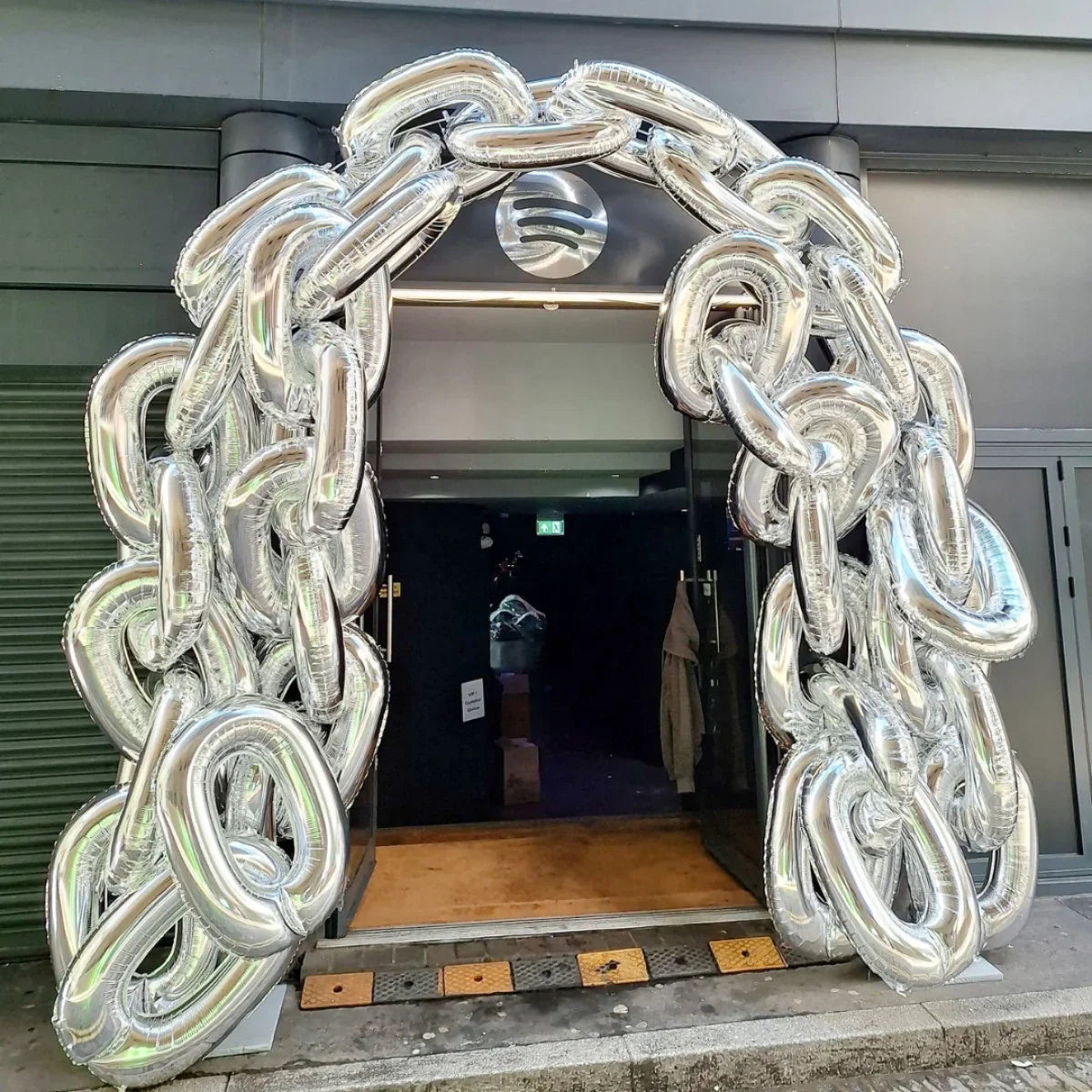 Silver metallic balloon arch shaped like large chain links at building entrance