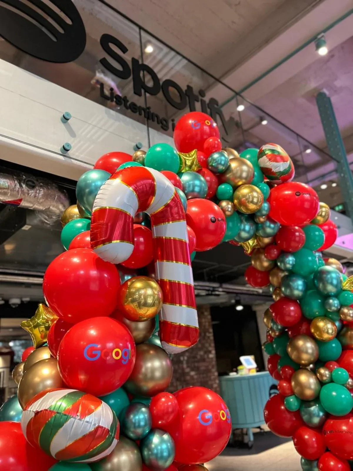 Festive balloon arch with red, green, gold balloons and candy cane decoration at Spotify office