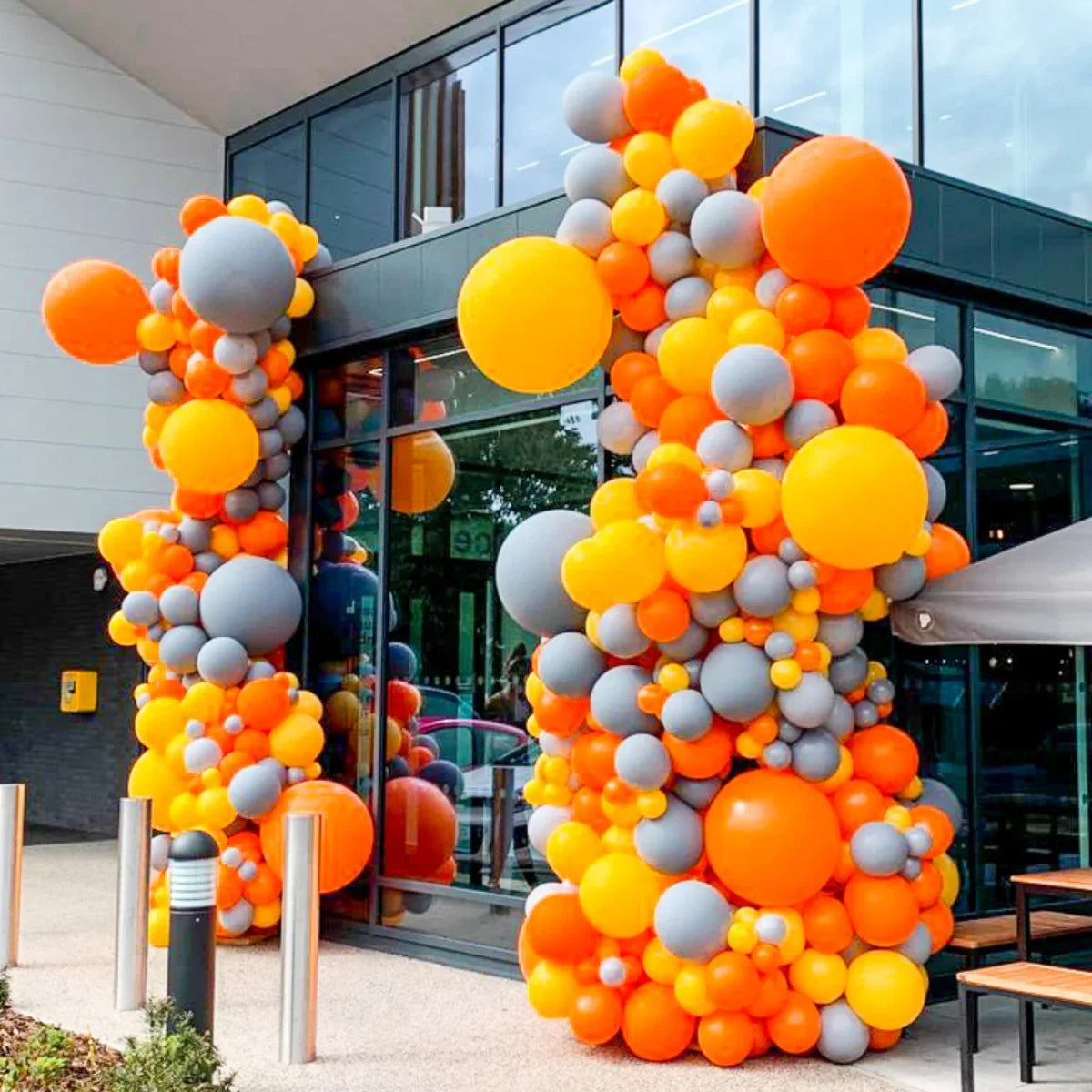 Outdoor corporate balloon installation with orange, yellow, and gray balloons at modern building entrance