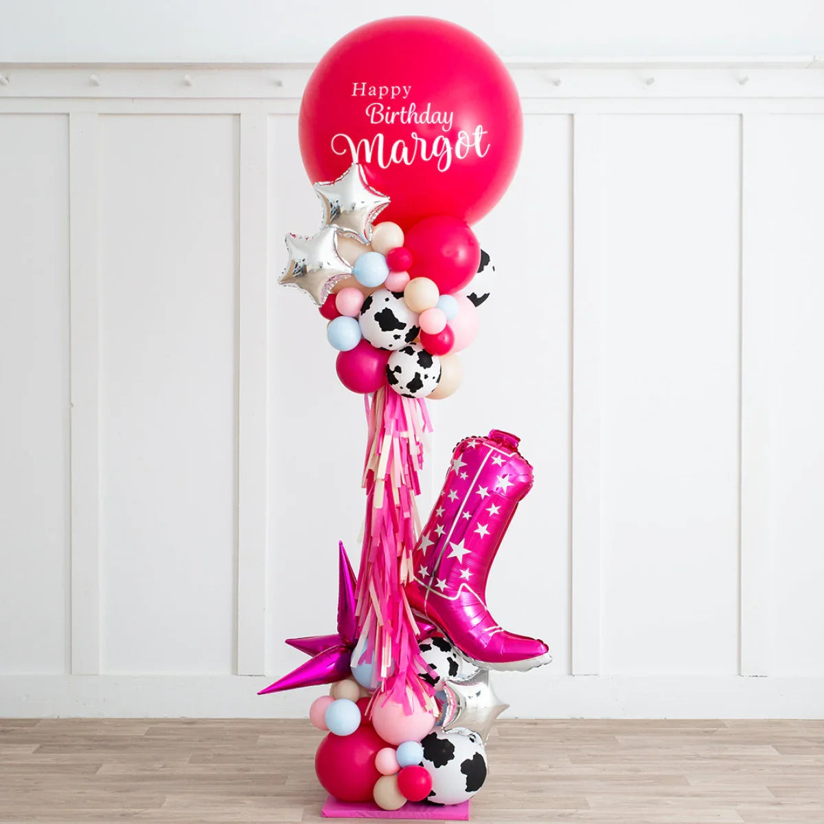 Colorful birthday balloon pillar with cowgirl boot, star foil balloons, and 'Happy Birthday Margot' red balloon