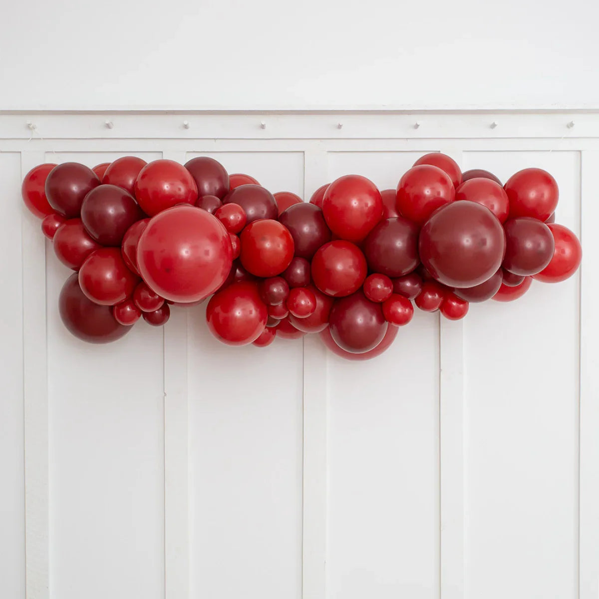 Dark cherry red balloon garland with various sizes hanging on white wall panel